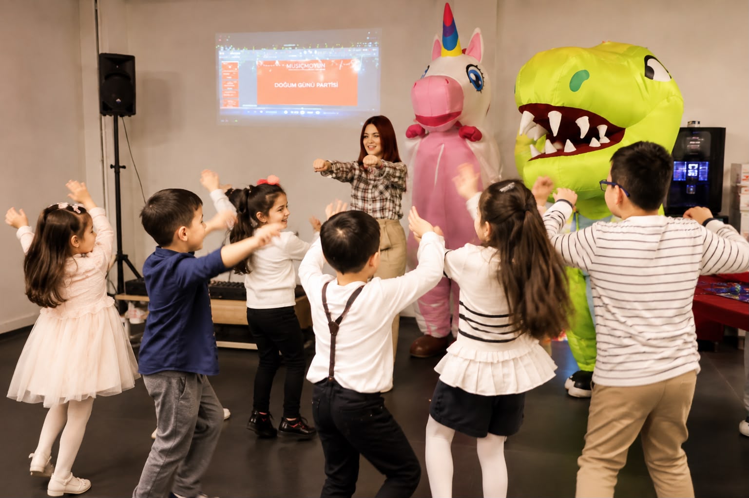 Unicorn ve dinozor maskotlarla dans eden çocuklar
